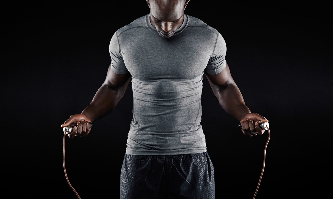 What does commitment mean: Muscular man skipping rope. Portrait of muscular young man exercising with jumping rope on black background